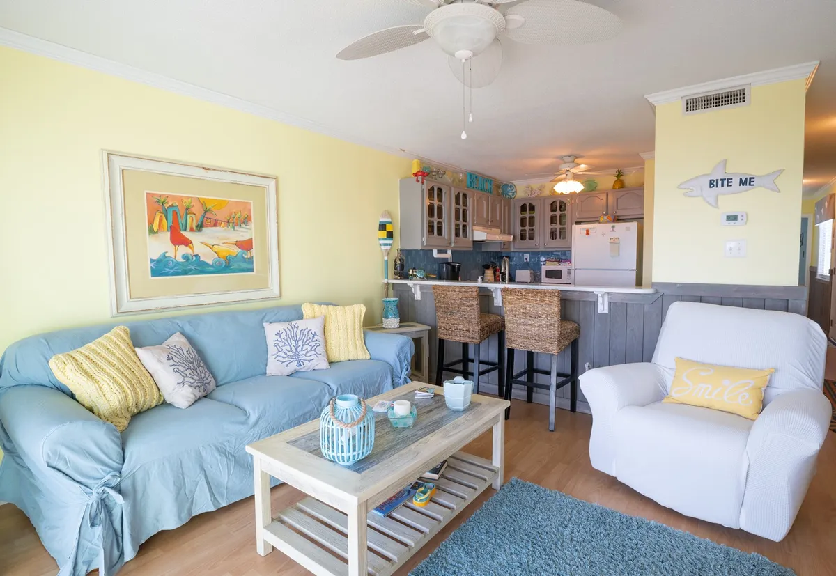 A welcoming living area with a light blue couch, colorful artwork, a wooden coffee table, and bar stools, all arranged to evoke a home-like and tranquil atmosphere ideal for relaxation or remote work.