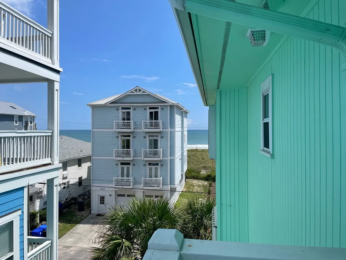 This image displays beachfront buildings lined with palm trees and a wide, open view of the ocean. The sandy coastline and inviting blue water create a natural, tranquil atmosphere perfect for relaxation by the sea. The buildings hint at a peaceful, small community situated right by the beach.