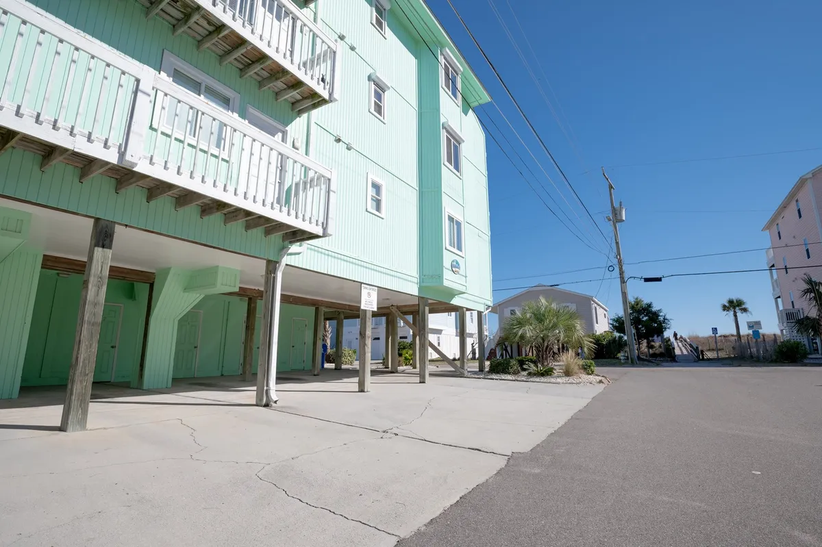 This exterior image showcases a green building with balconies bordered by palm trees, evoking a warm and inviting vibe. The presence of balconies and nearby greenery hints at both community and easy access to outdoor relaxation.