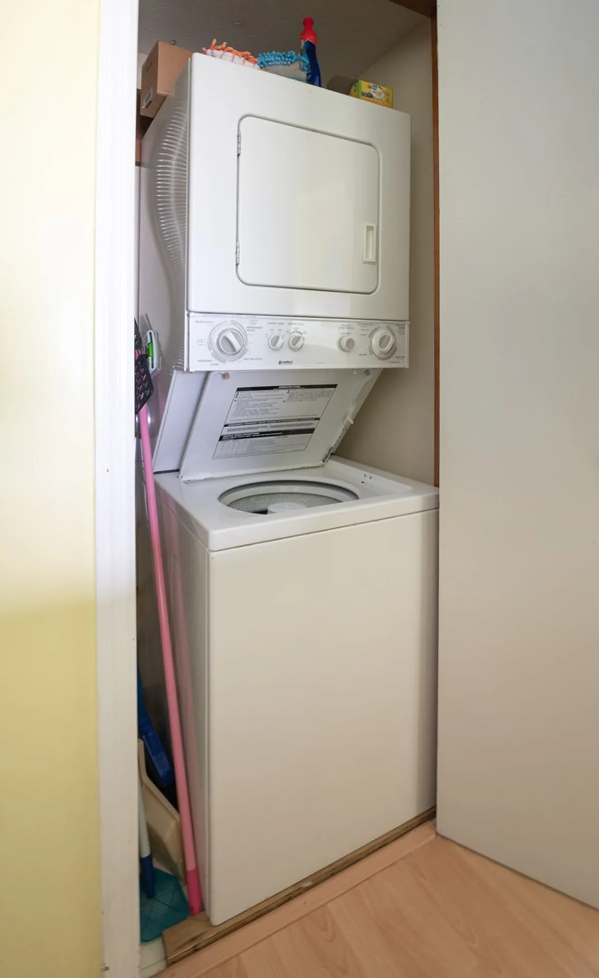 A neatly arranged laundry closet featuring a stacked washer and dryer, with cleaning supplies organized on top. The area looks tidy and user-friendly, highlighting the convenience of in-unit laundry.