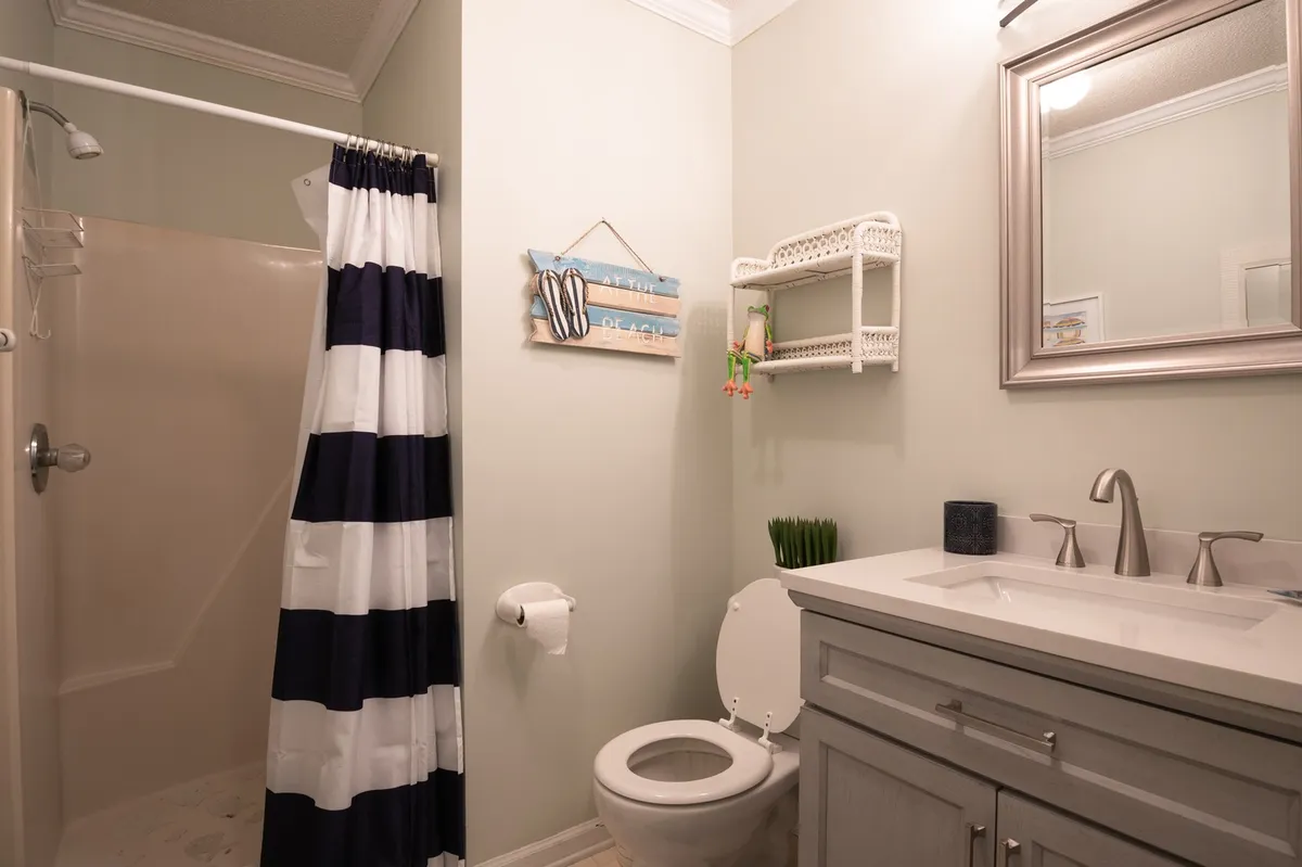A modern bathroom with a striped shower curtain, sleek vanity, and a framed mirror. The space is clean, bright, and inviting, ideal for refreshing showers and self-care routines.