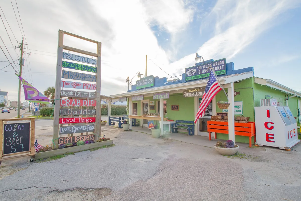 This image features the brightly painted exterior of a local market or eatery, with a signboard listing menu items and an American flag, evoking a community hub atmosphere. The inviting façade and signage suggest a place where visitors can purchase local produce, grab artisanal coffee, or enjoy a quick meal.