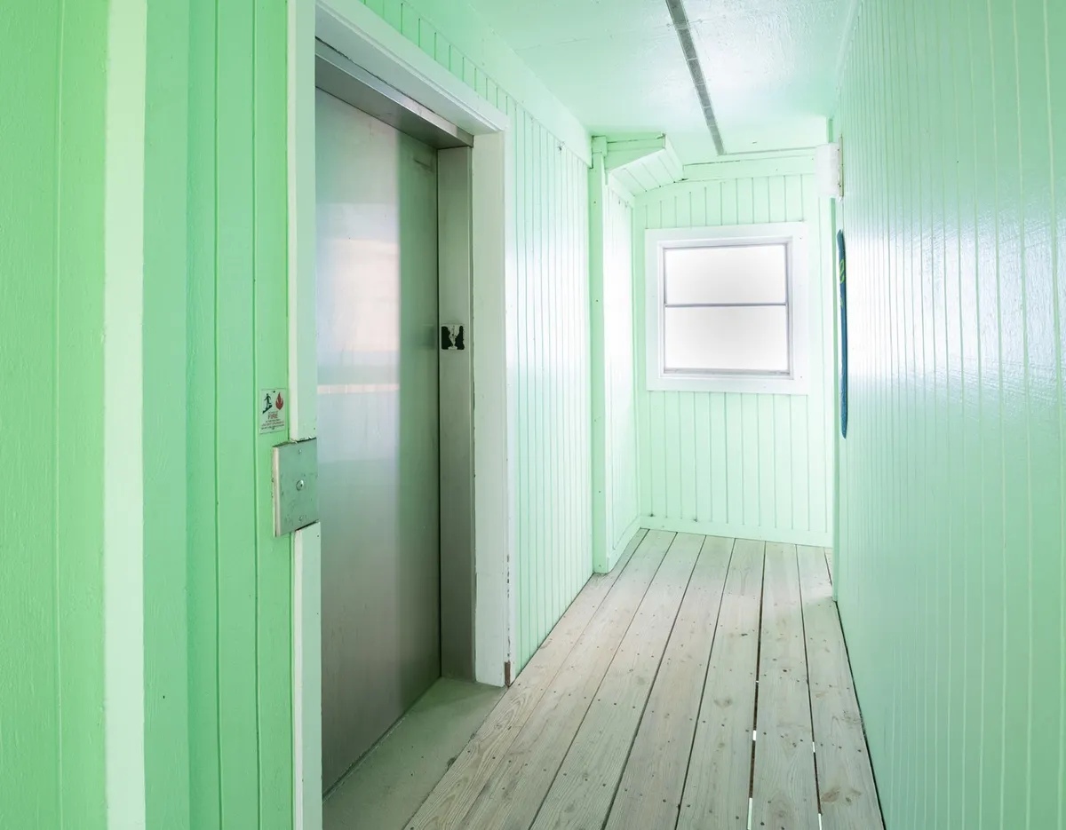 A small elevator within the building, featuring textured walls and a window that lets in natural light. The area appears cozy and accessible for guests with luggage or groceries.